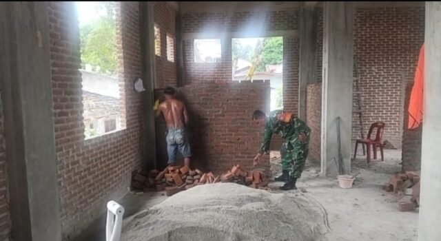 Wujudkan Kemanunggalan TNI-Rakyat, Babinsa Kuta Timu Bantu Pengerjaan Kantor Keuchik